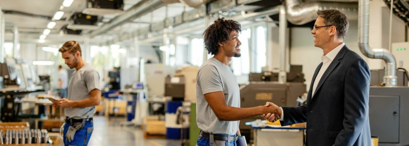 Mann in Arbeitskleidung schüttelt Mann in Anzug die Hand