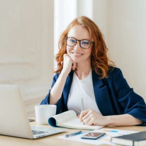 Frau mit roten Haaren sitzt vor Laptop und lächelt