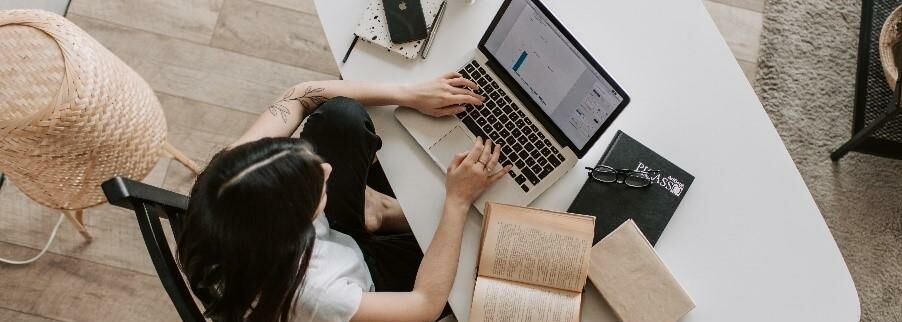 Junge Frau sitzt an Schreibtisch und arbeitet auf Laptop