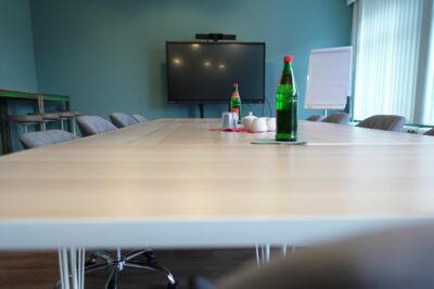 Langer Tisch mit Stühlen, im Hintergrund hohe Tische mit Barhockern, Smartboard und Flipchart