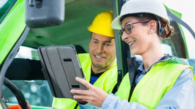 Mann in Fahrzeug daneben Frau mit Tablet