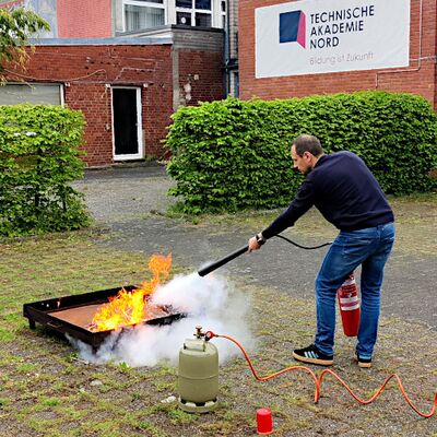 Ein Mann mit einem Feuerlöscher löscht eine Flamme, die in einer Feuerschale brennt.