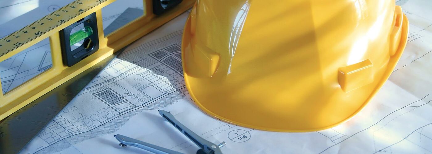 Helm, Wasserwaage und Zirkel auf Bauplan
