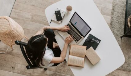 Junge Frau sitzt an Schreibtisch und arbeitet auf Laptop
