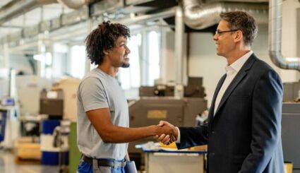 Mann in Arbeitskleidung schüttelt Mann in Anzug die Hand