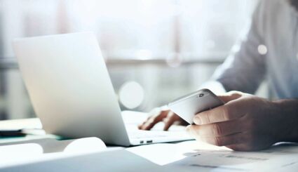 Mann mit Smartphone in der Hand sitzt an Laptop
