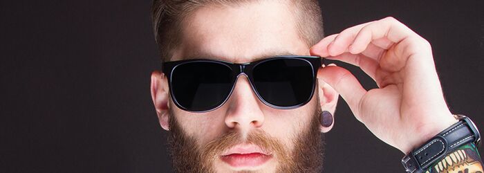 Mann mit Bart, Sonnenbrille, Hemd und Fliege vor schwarzem Hintergrund schaut in die Kamera