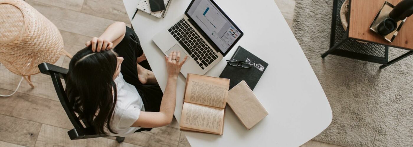 Junge Frau sitzt an Schreibtisch und arbeitet auf Laptop